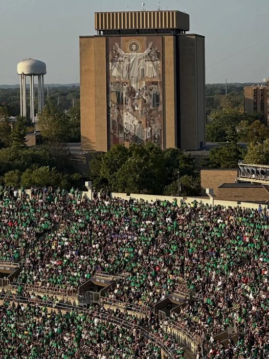 Notre Dame Stadium on game day with Hesburgh Library's Word of Life mural in the background